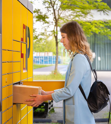 Frau gibt an einem Paketautomat ein Paket auf